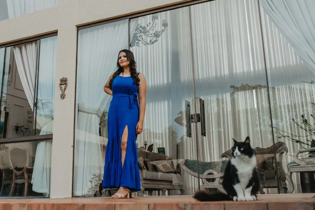 Jovem de vestido azul diante de portas de vidro, com um cão ao lado.