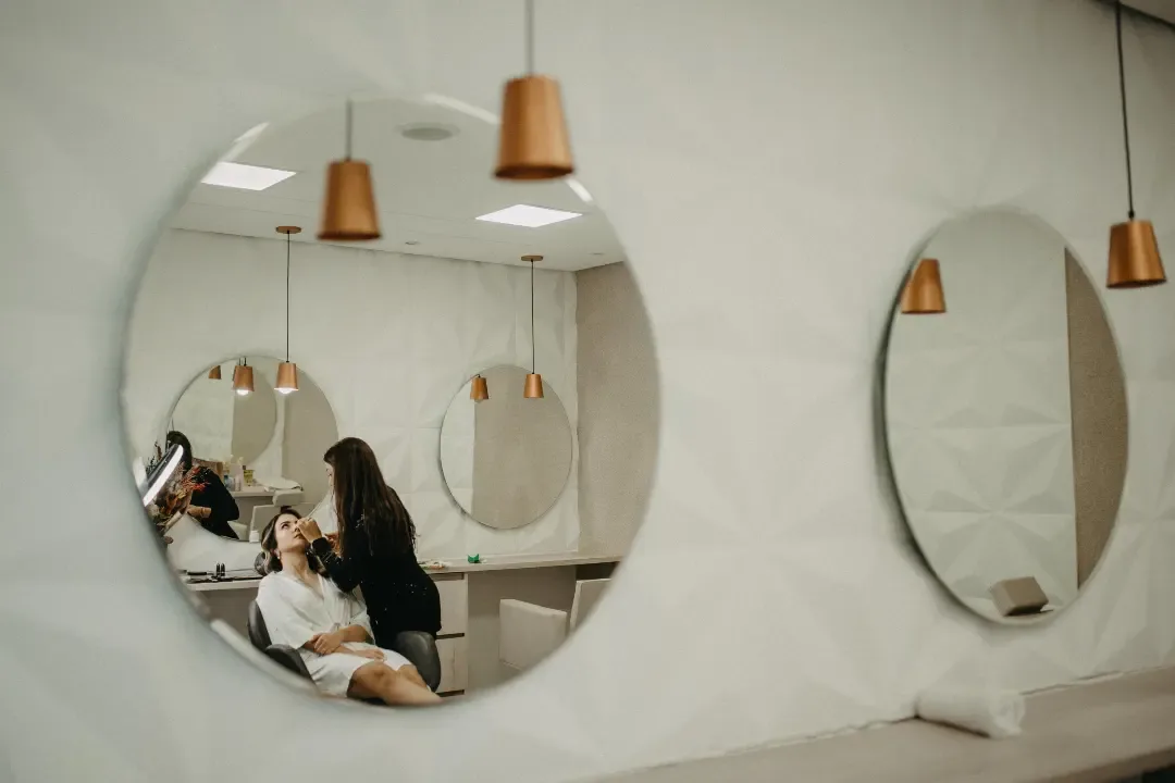Noiva e outra mulher refletidas em espelhos redondos de uma sala clara.