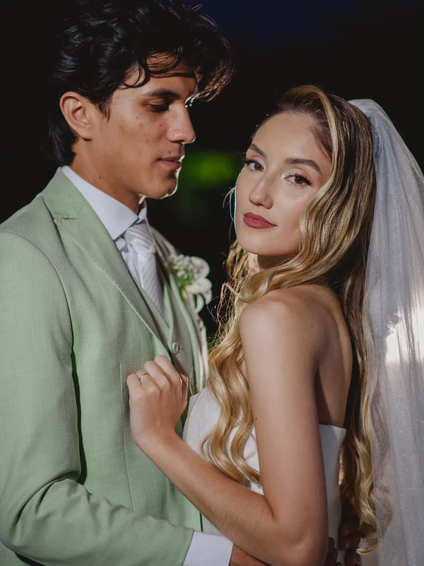 Casal de noivos abraçado diante de um fundo escuro.