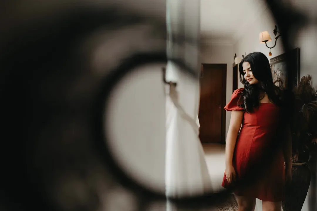 Jovem de vestido vermelho refletida em um espelho.