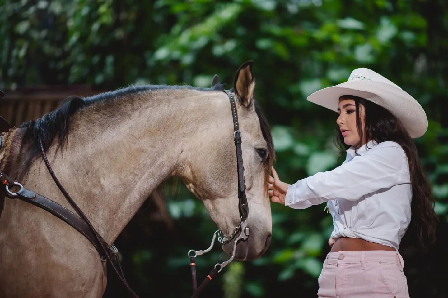 Jovem de chapéu e camisa clara ao lado de um cavalo.