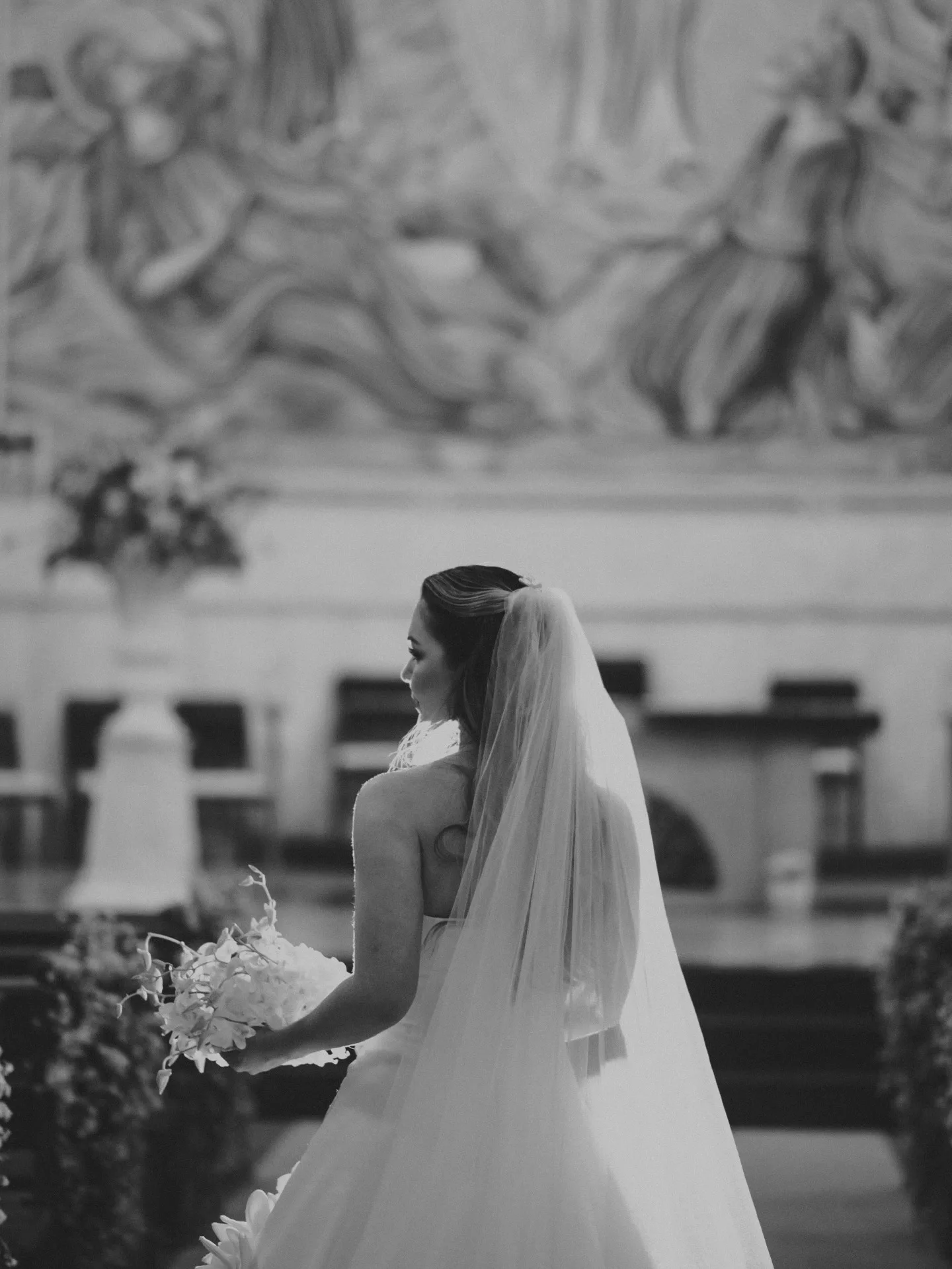 Noiva de costas dentro da igreja, em fotografia em preto e branco.