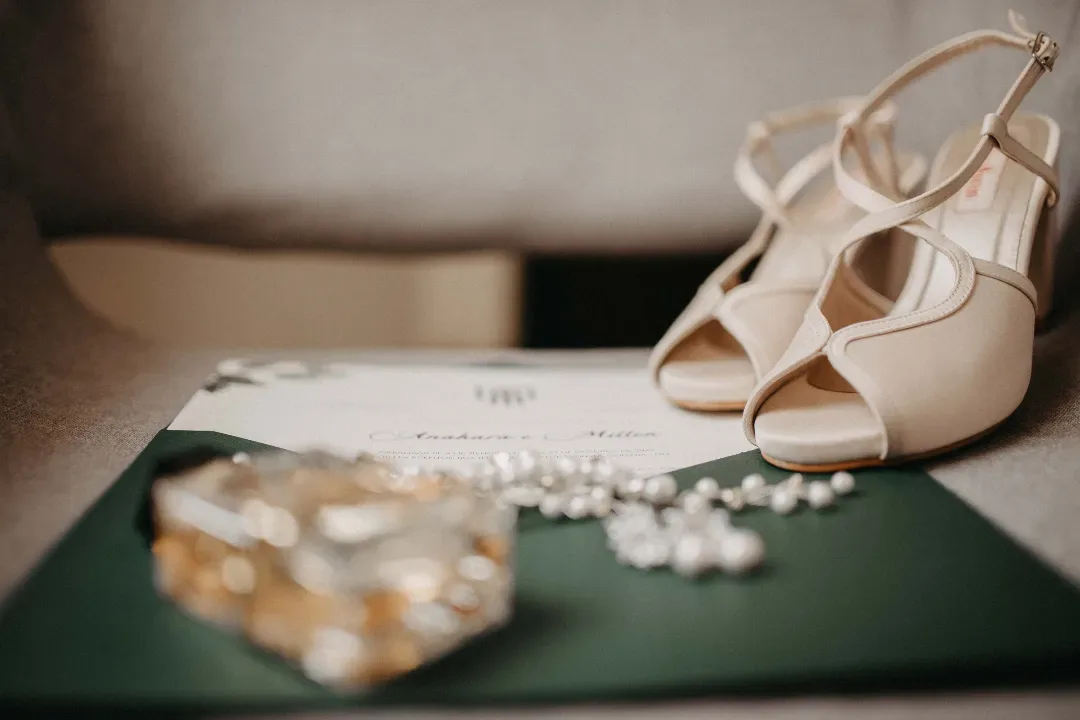 Sapatos claros e acessórios da noiva sobre uma superfície verde.