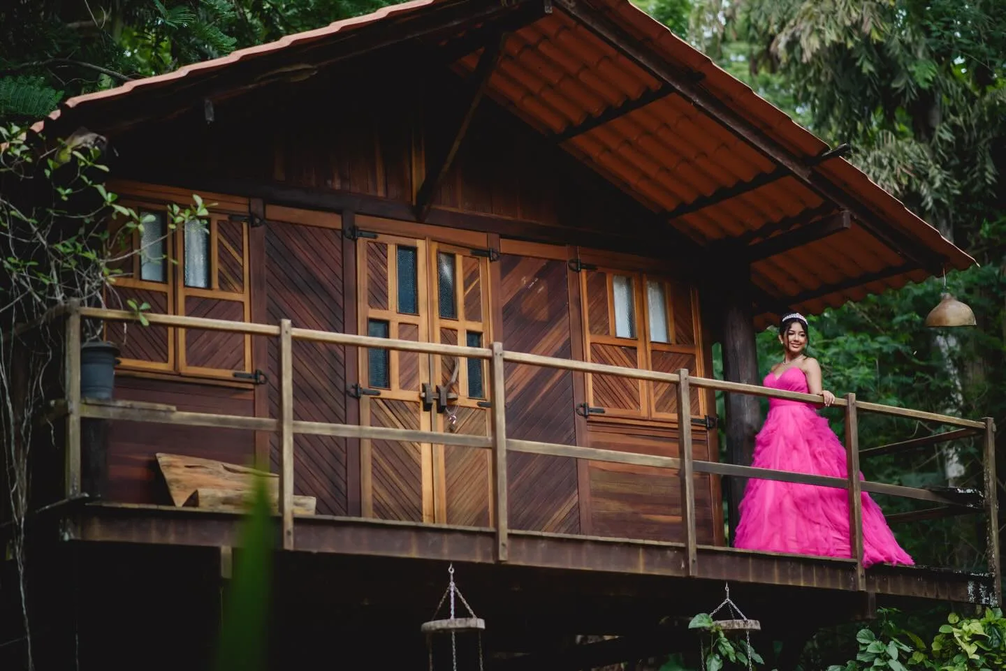 Jovem de vestido rosa na varanda de uma casa de madeira.