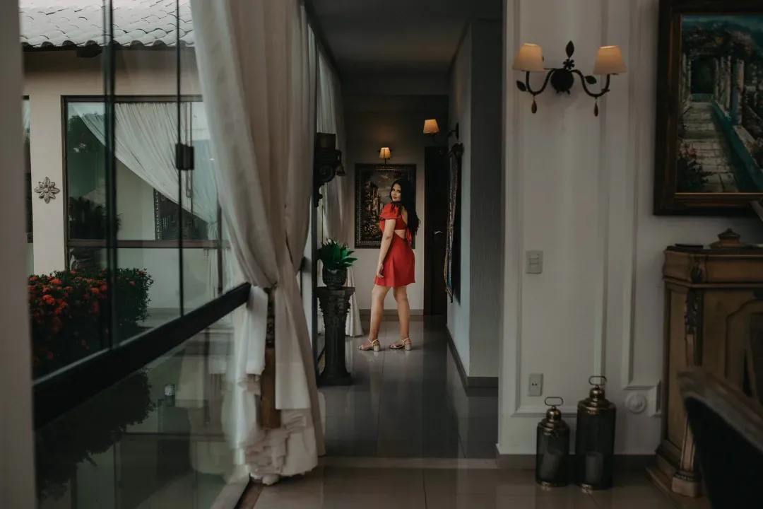 Jovem de vestido vermelho ao fundo de uma sala com espelhos.