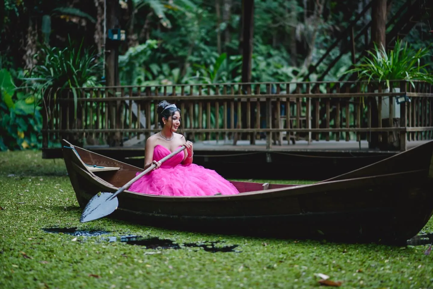 Jovem de vestido rosa sentada em um barco sobre a grama.
