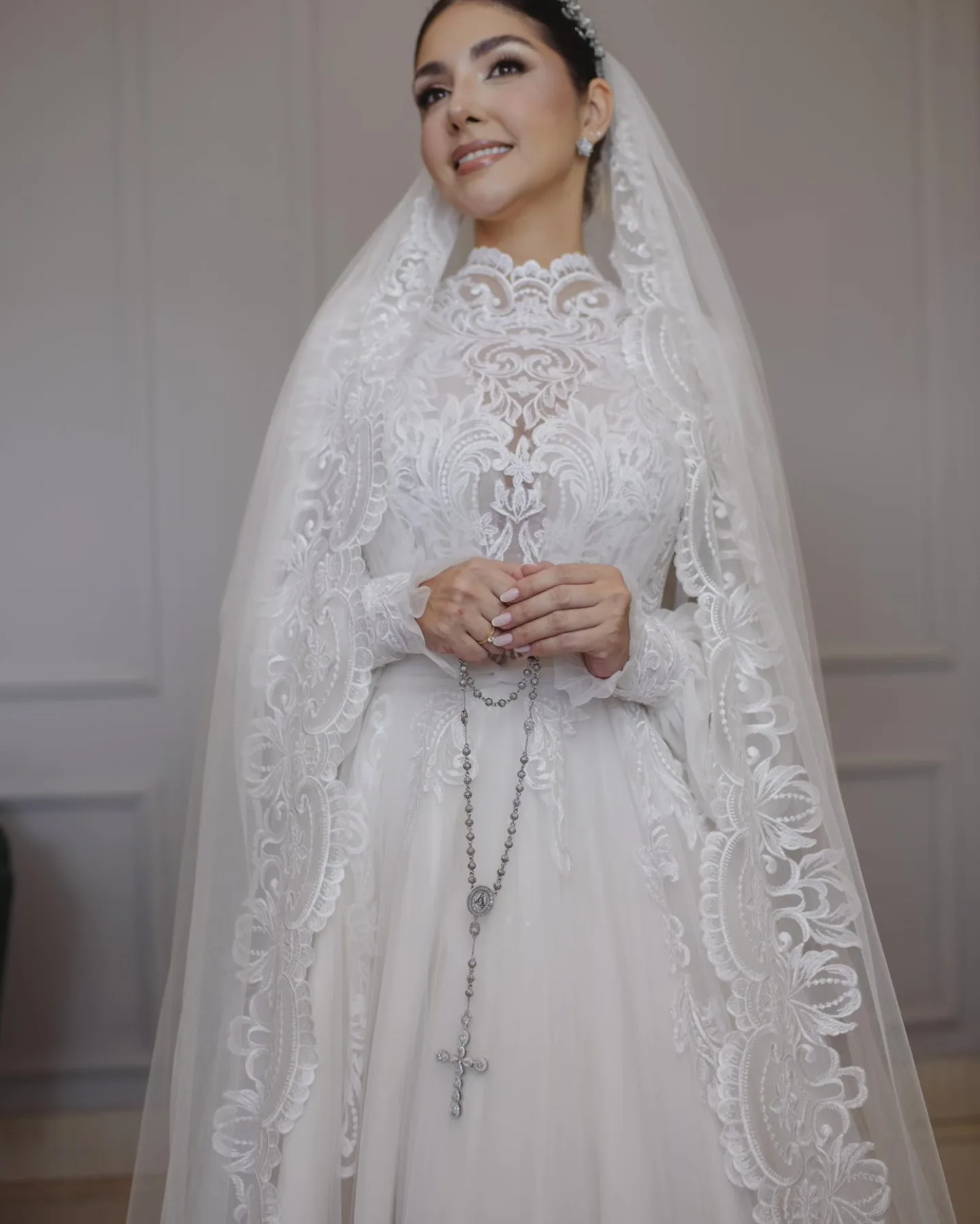 Noiva sorrindo com as mãos unidas sobre o vestido rendado.
