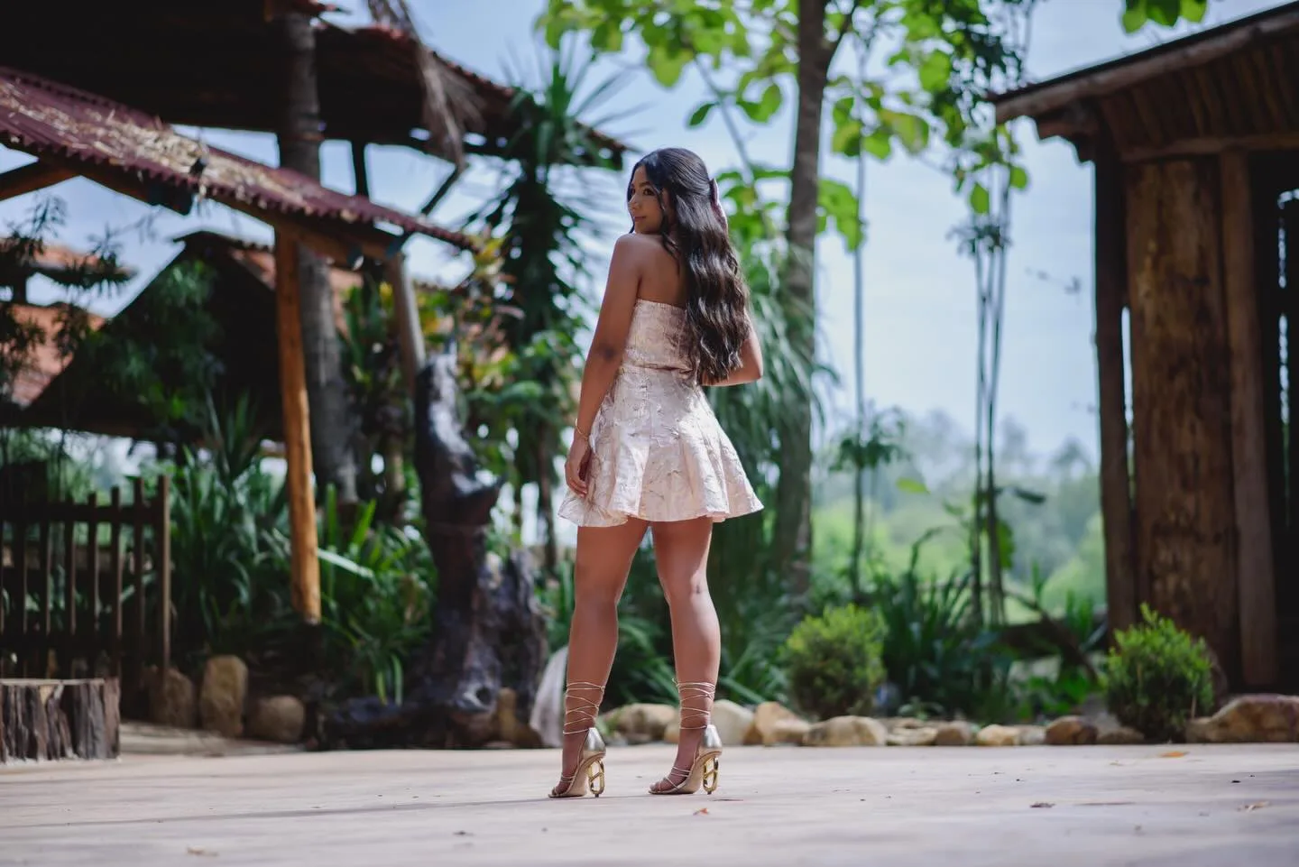 Jovem de vestido curto caminhando diante de uma casa de madeira.