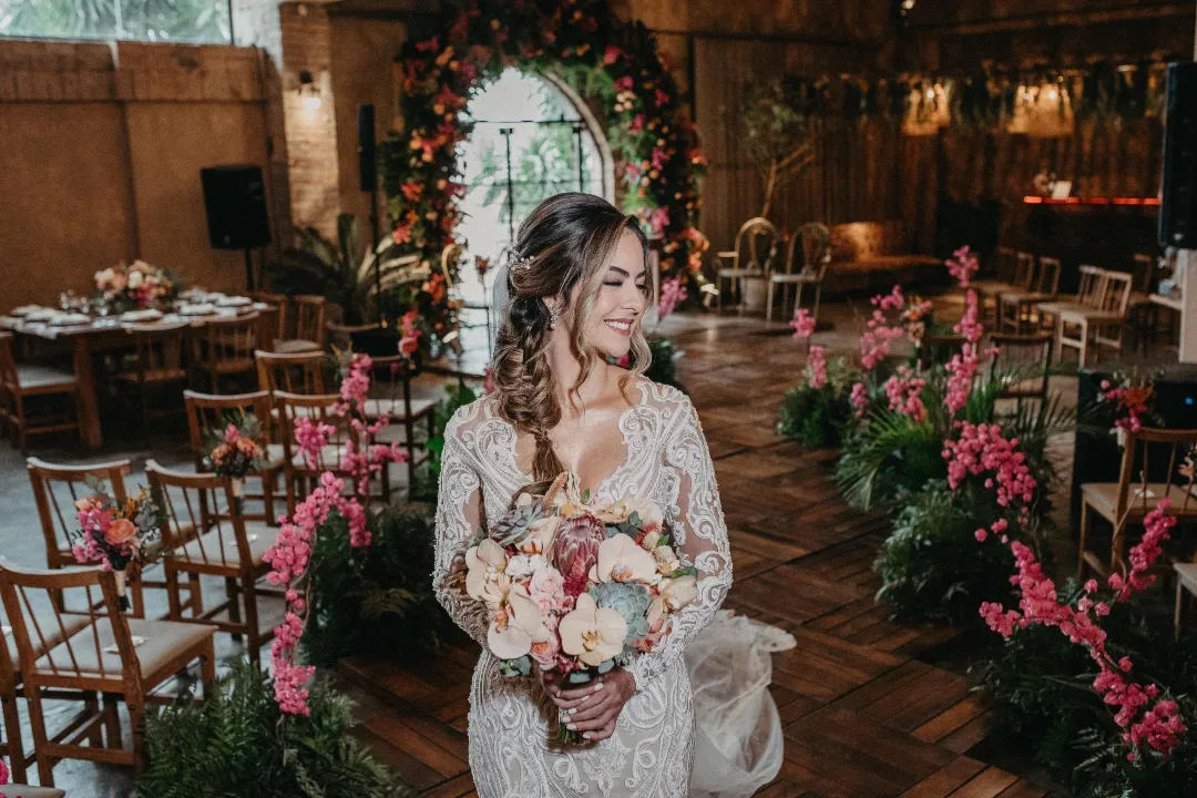 Noiva segurando o buquê entre cadeiras e arranjos florais.