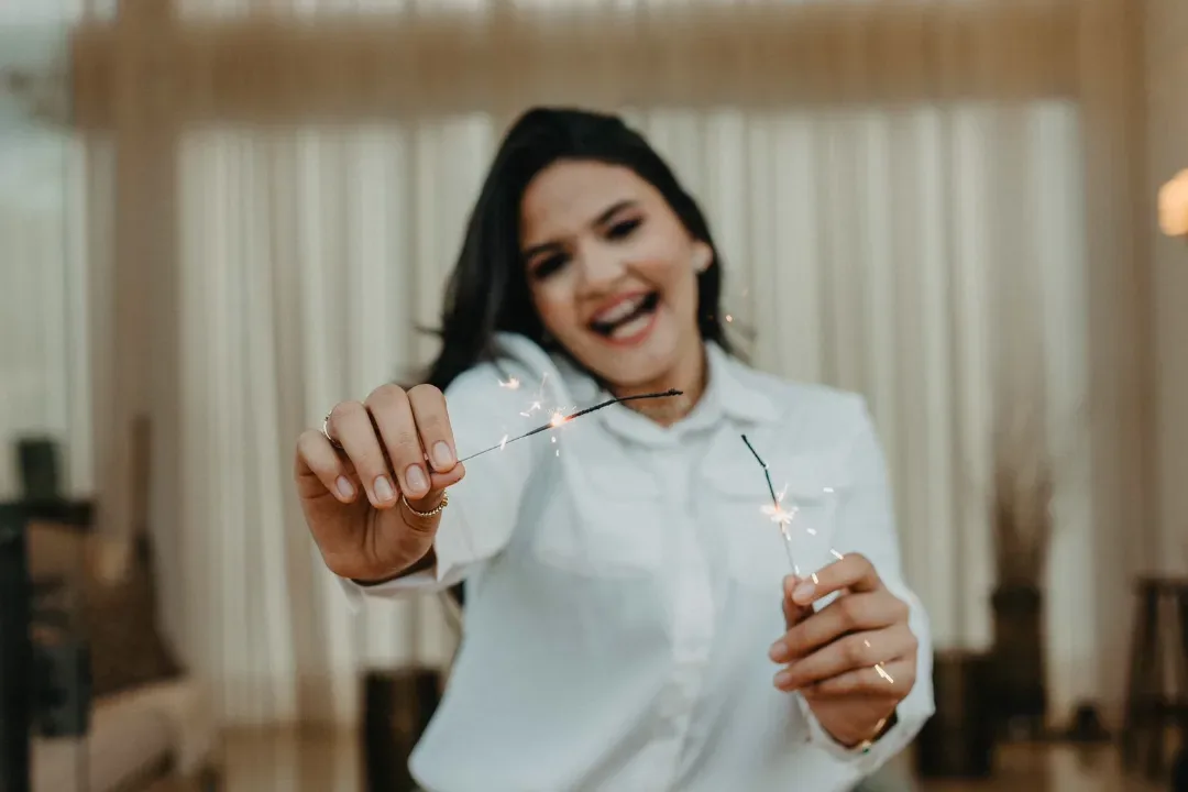 Jovem de camisa branca sorrindo diante de uma cortina.