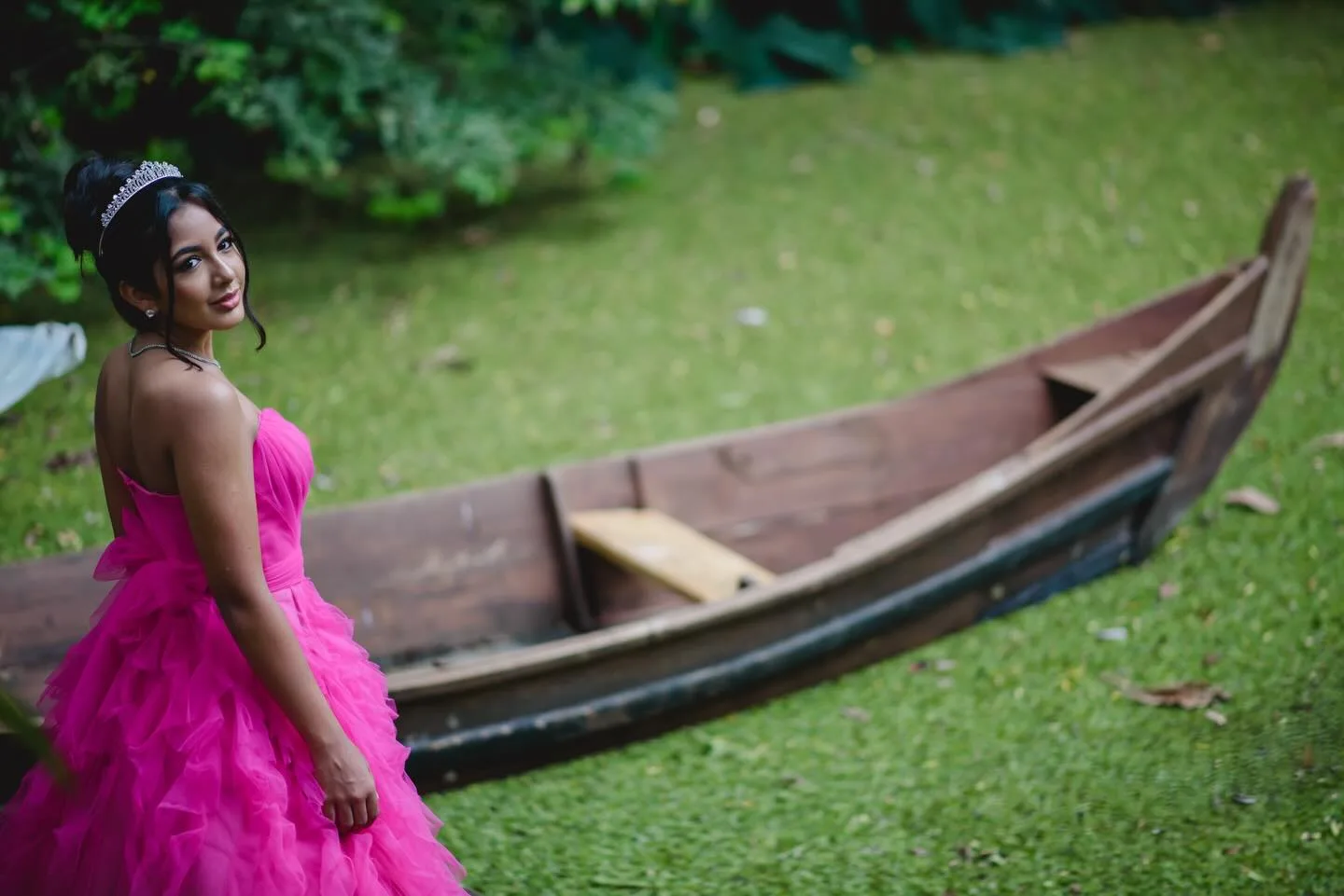 Jovem de vestido rosa junto a um barco no jardim.