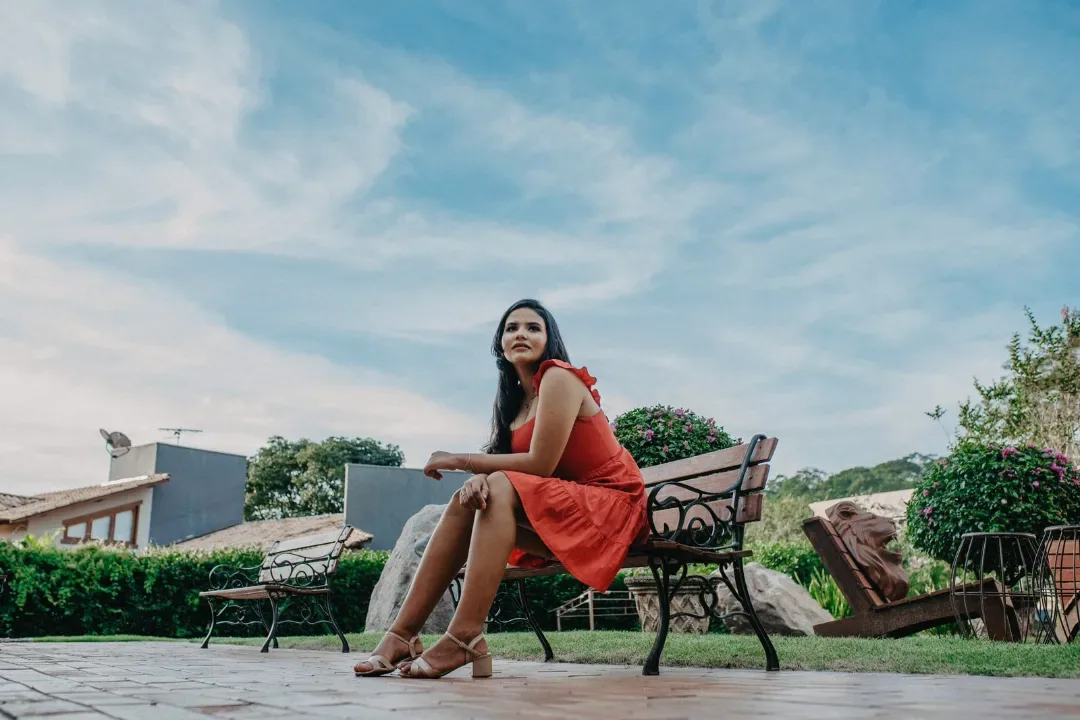 Jovem de vestido vermelho sentada em um banco ao ar livre.