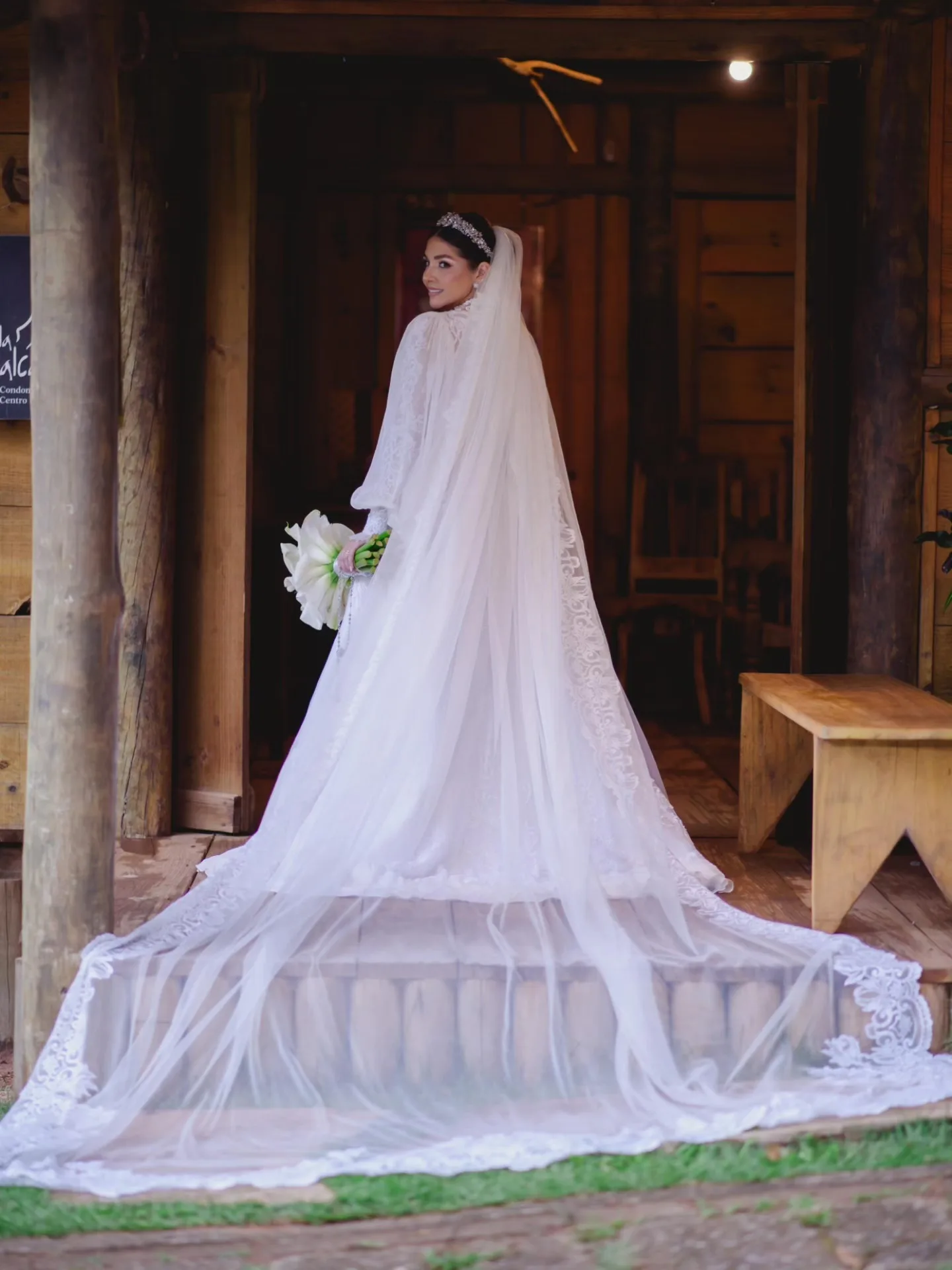 Noiva de véu longo diante de uma porta de madeira.