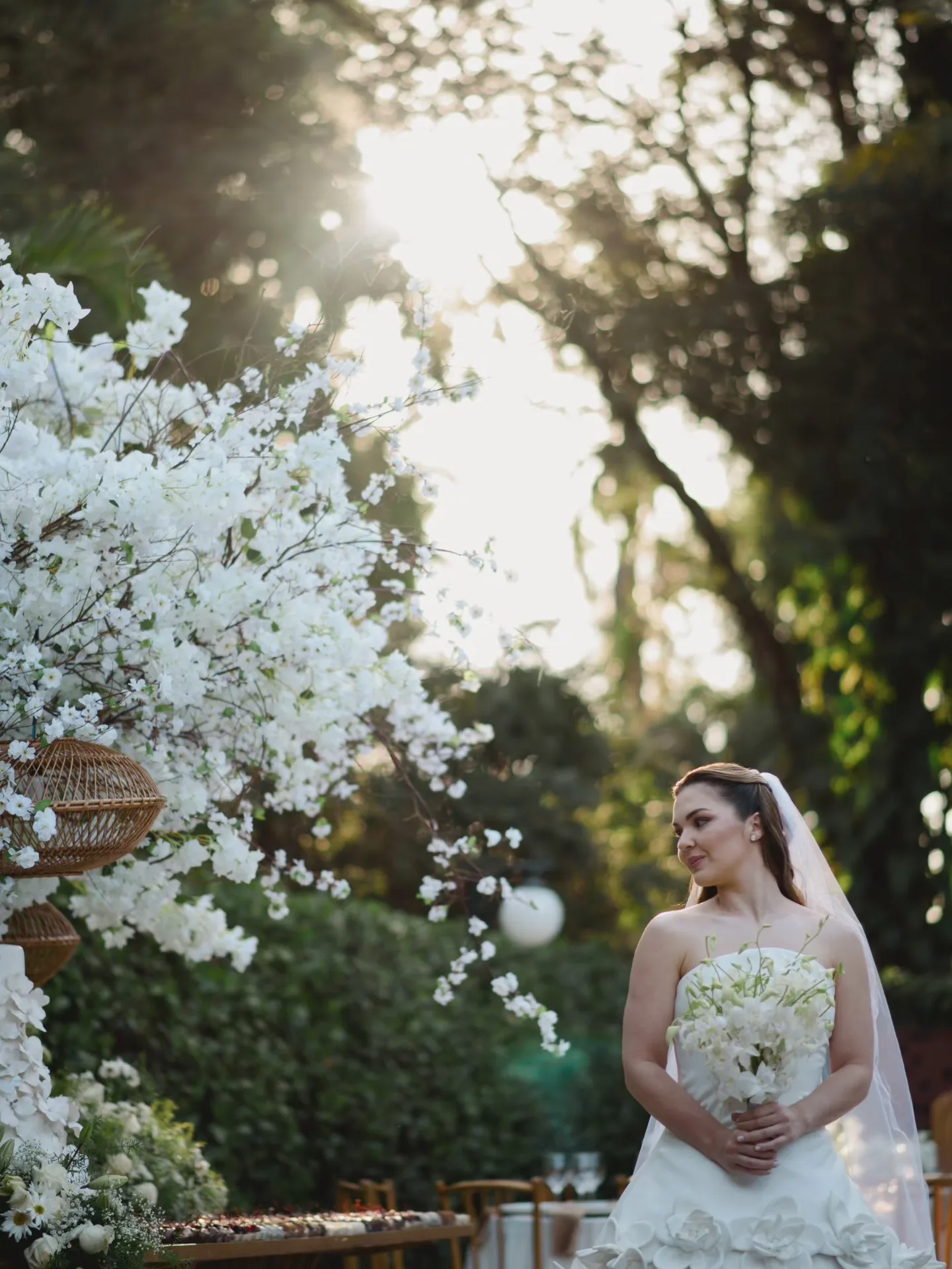 Noiva segurando o buquê junto a flores brancas no jardim.