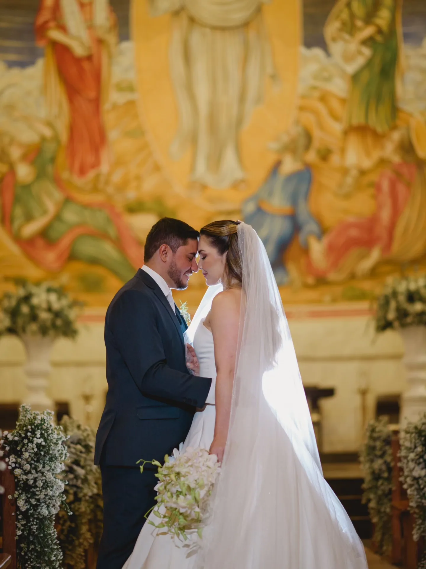 Noivos se beijando diante de um painel colorido de igreja.