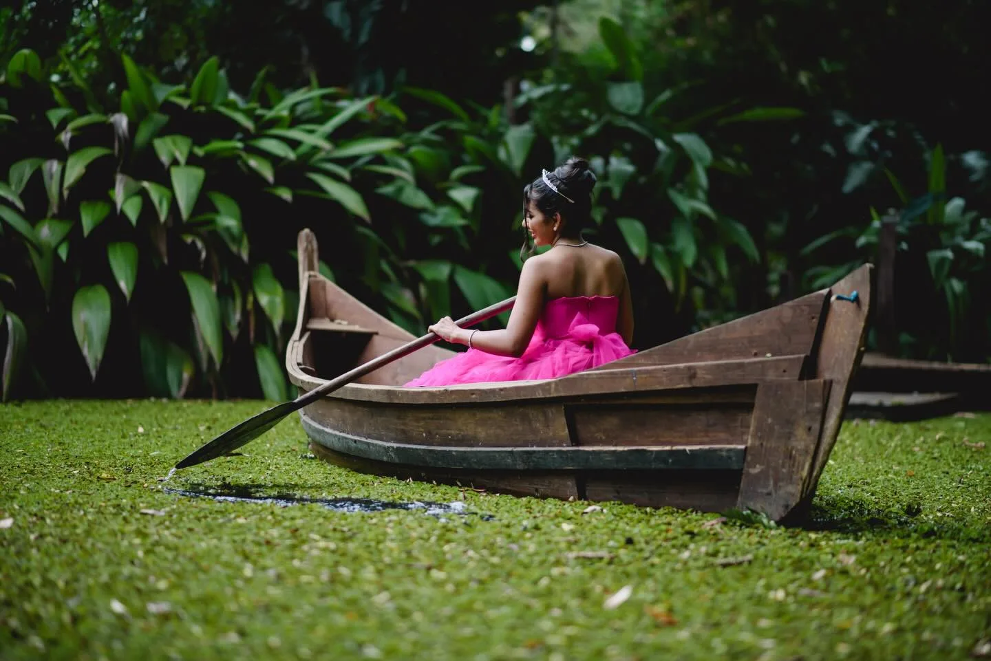 Jovem de vestido rosa sentada em um barco cercado por vegetação.
