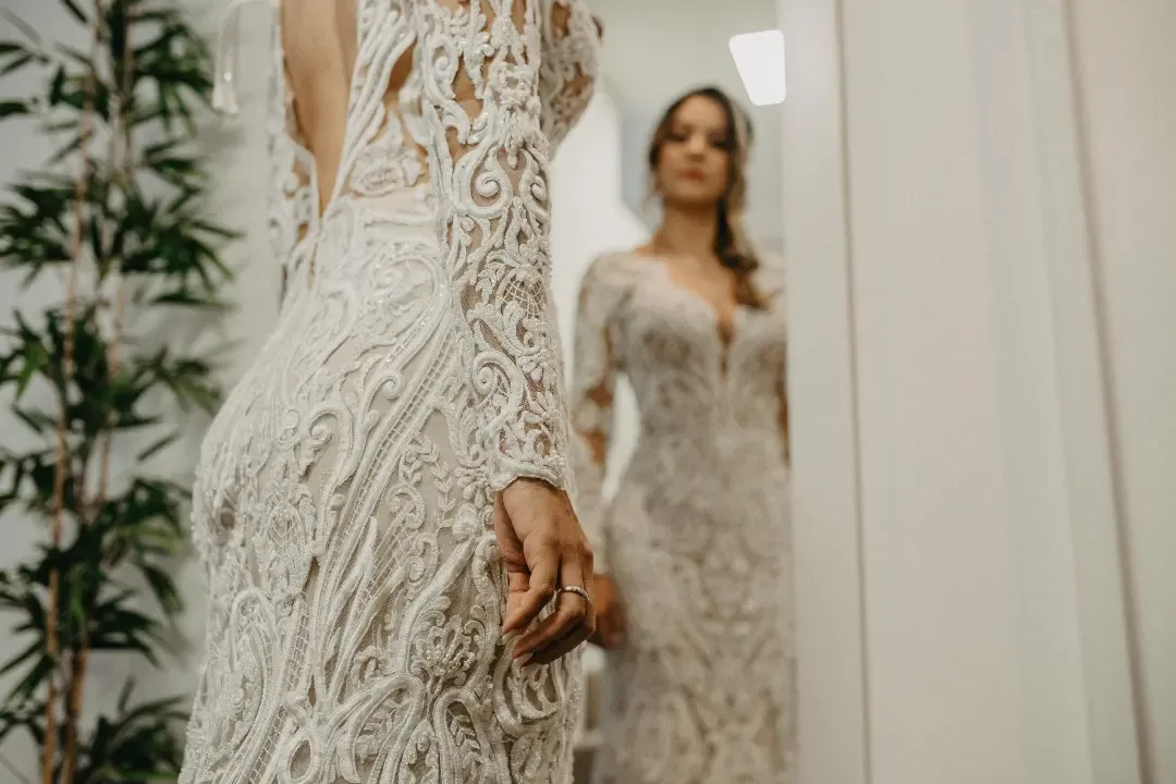 Detalhe do vestido rendado com a noiva ao fundo.
