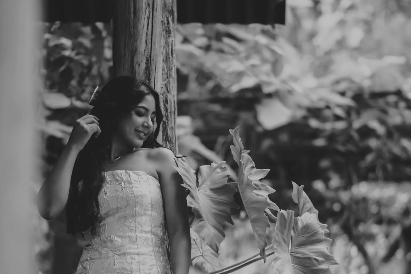 Jovem de vestido sem alças junto à vegetação, em preto e branco.